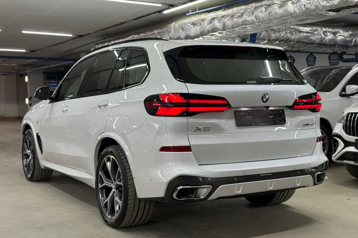 سيارة BMW X5 بيضاء مصورة من الخلف بزاوية ثلاثية الأرباع في موقف سيارات تحت الأرض وبجانبها سيارات أخرى